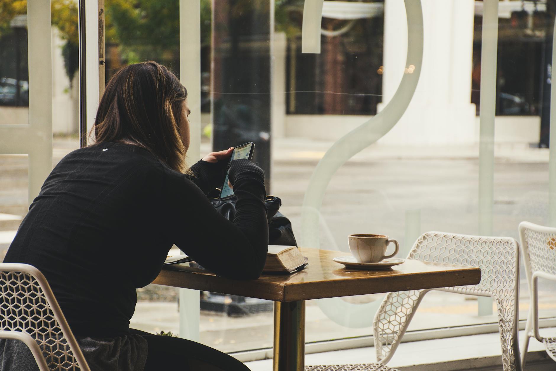 Woman using a smartphone while drinking coffee at a cafe table