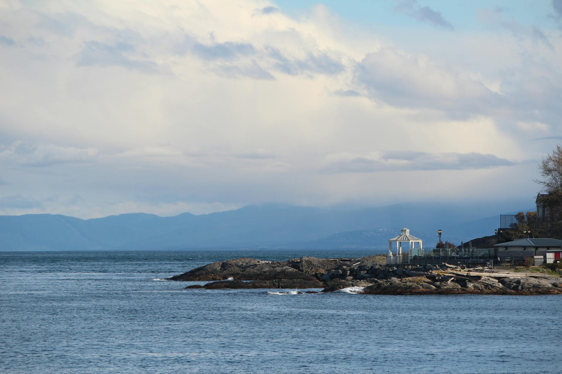 Rocky Victoria coastline with distant mountains under cloudy sky