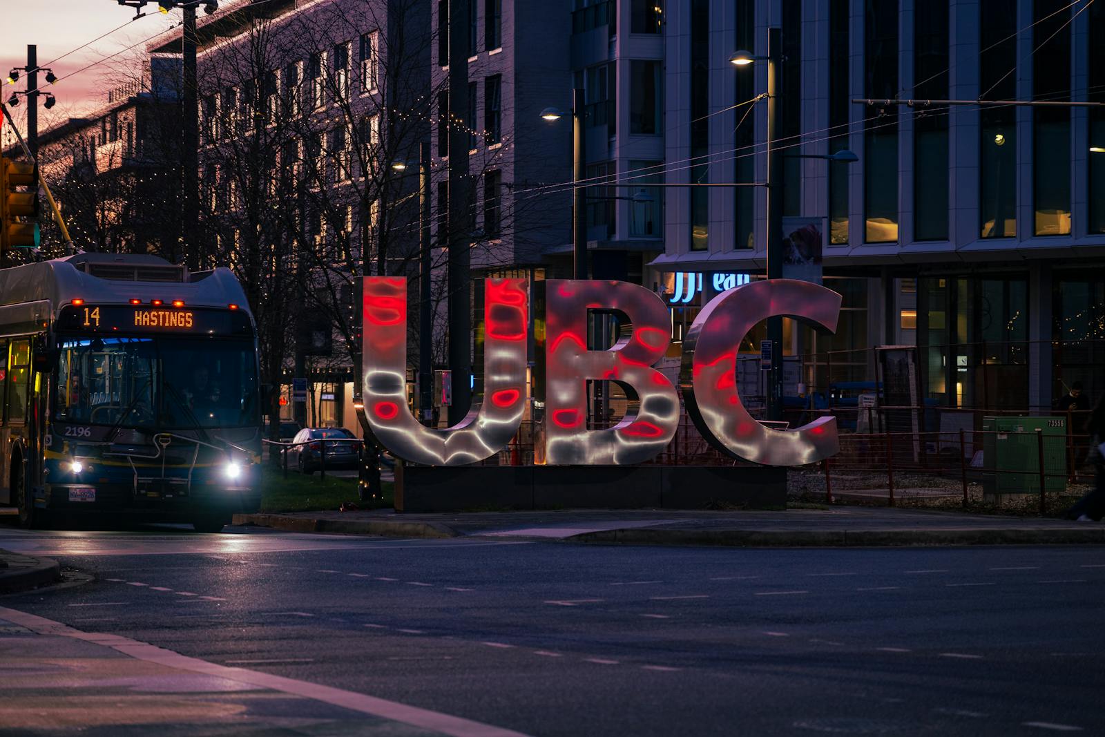 Evening scene of UBC sign illuminated with city bus at University Endowment Lands in Vancouver, BC.