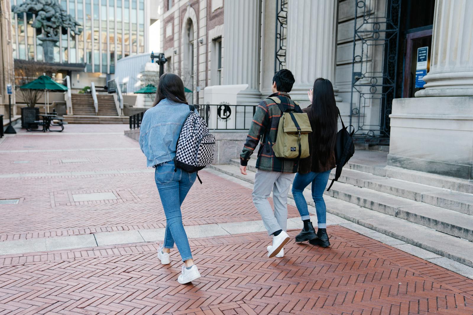 A group of young students walk along a university campus pathway, carrying backpacks.