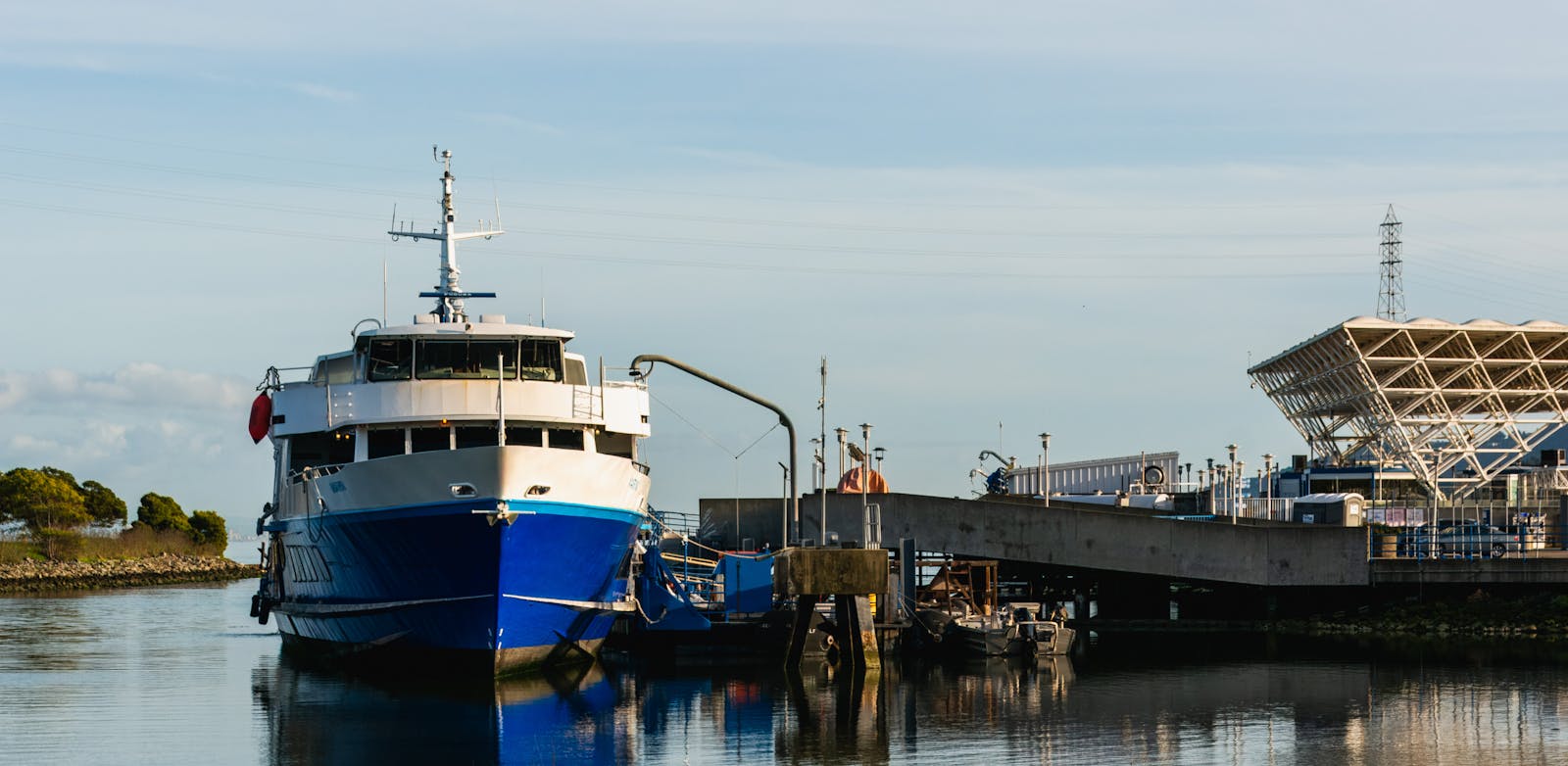 Large blue passenger ship docked at a modern harbor terminal during the day.
