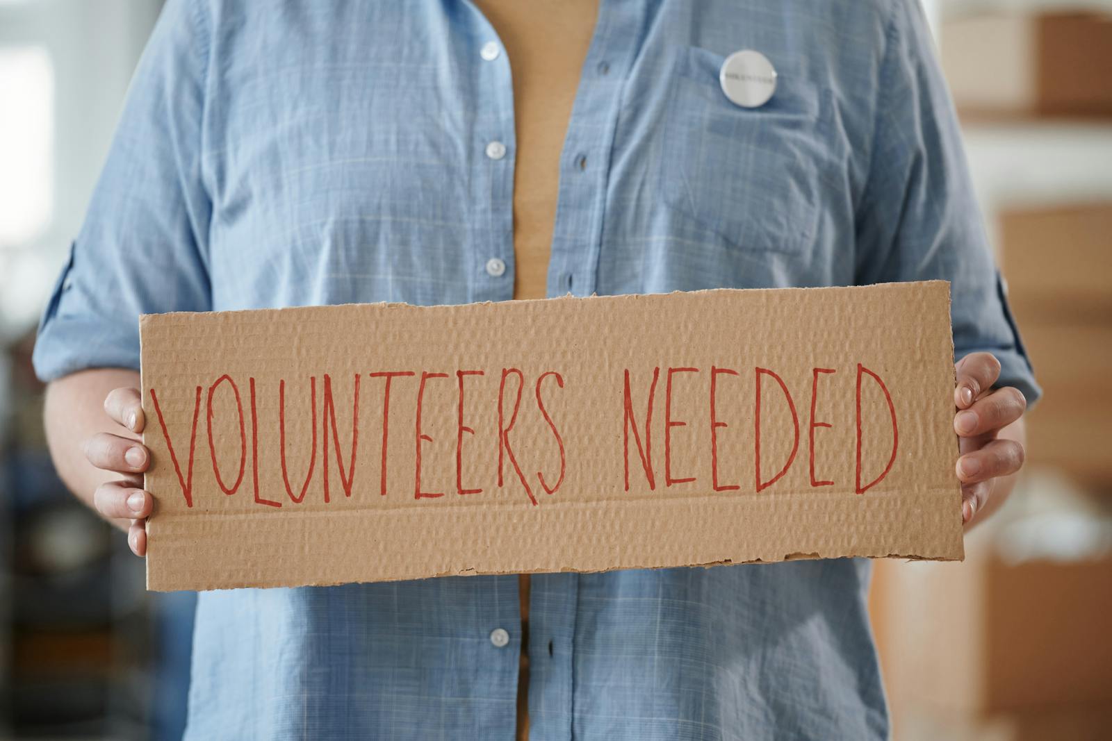 Person holding a sign reading Volunteers Needed to encourage community support.