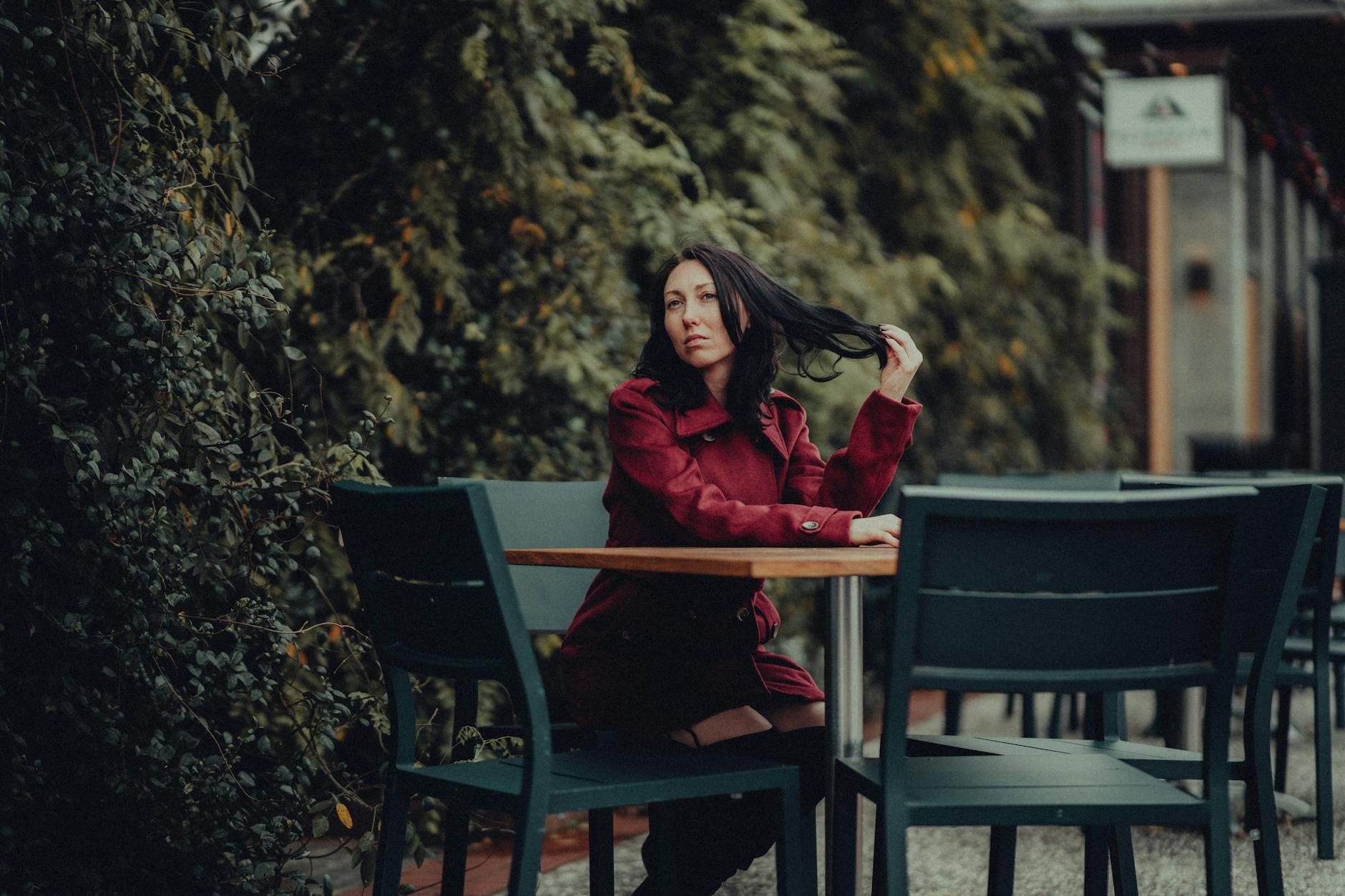 Woman in a red coat sitting at a cafe surrounded by greenery