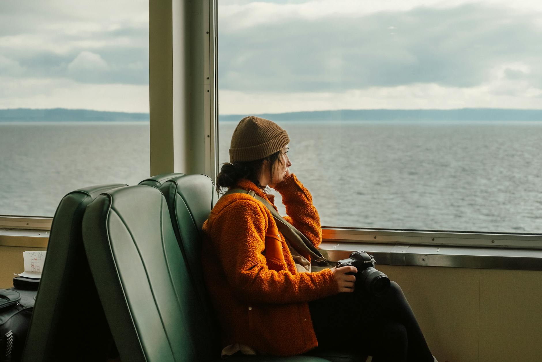 Woman looking out a ferry window with a camera in hand