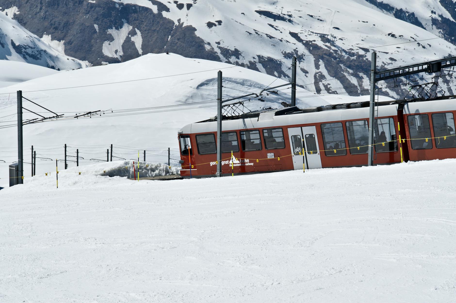 Red train in snowy Swiss Alps for older traveler Zermatt report planning.