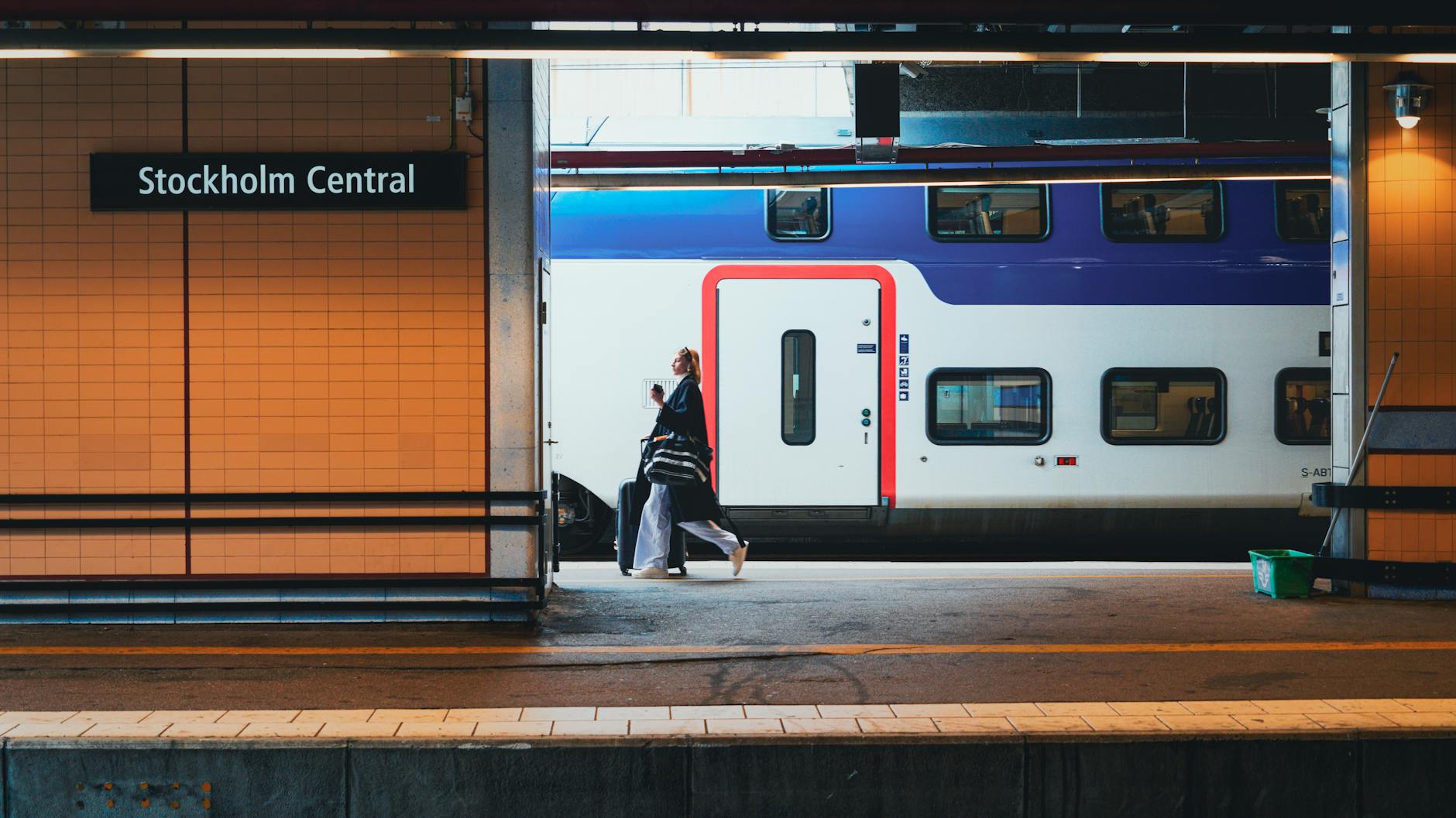Traveler with luggage beside a train at Stockholm Central.