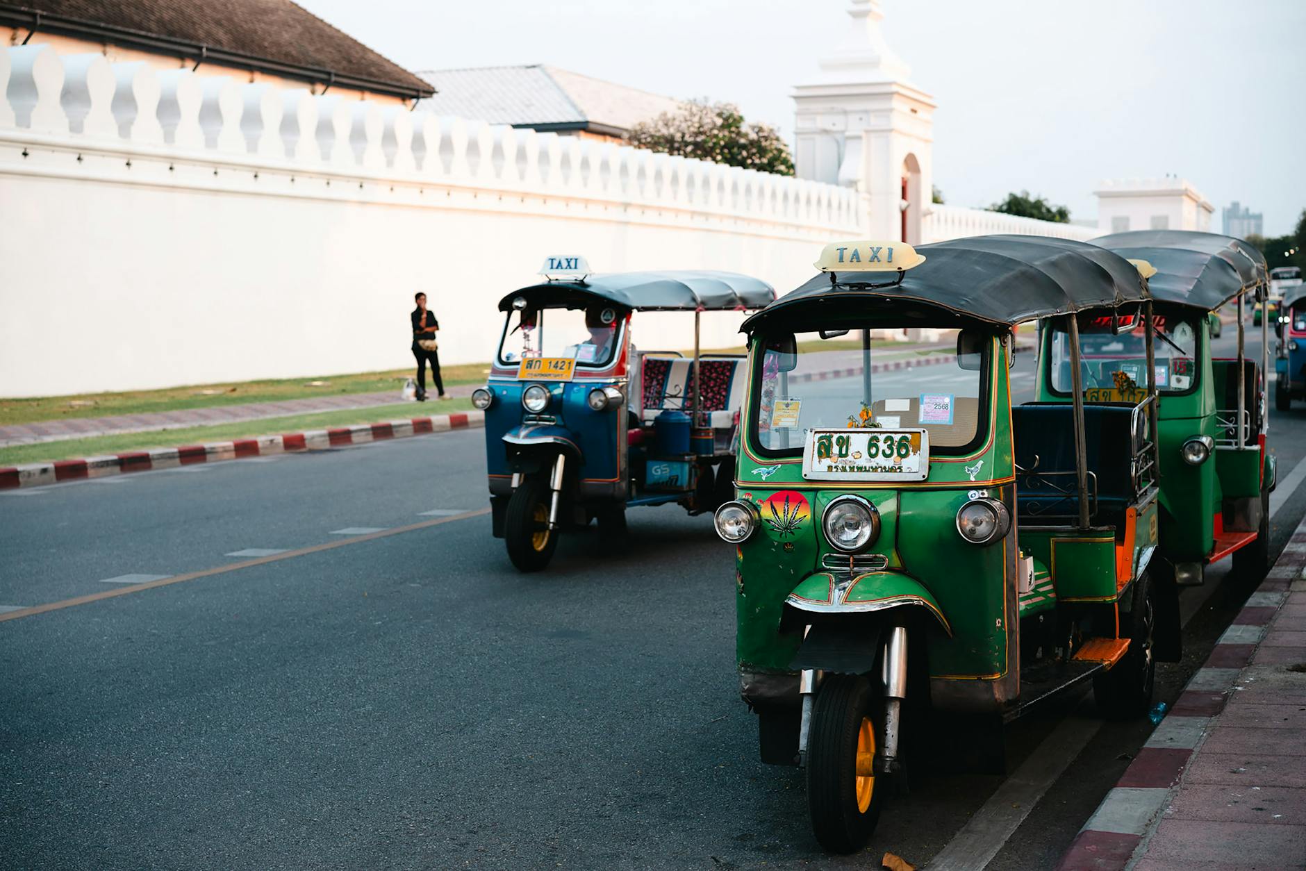 Green tuk-tuks waiting beside a Thai waterfront.